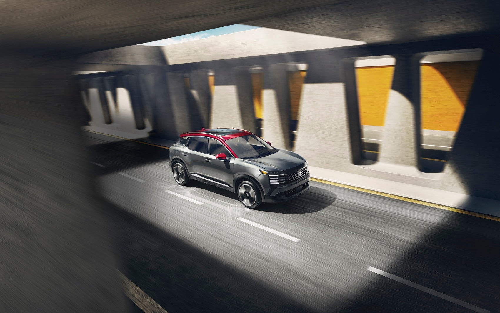 Nissan Kicks exterior front profile driving beside a yellow wall in sunlight

